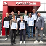 Gruppenfoto der Jubilarinnen und Jubilare mit ihren Ehrenurkunden und den Geschäftsführern Dennis Ochmann und Dirk Rutenhofer vor dem WECKBACHER Sicherheitszentrum NRW in Dortmund.