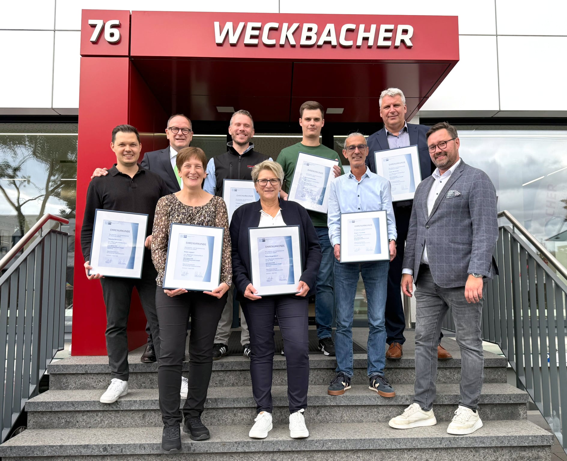 IMG_6771 Gruppenfoto der Jubilarinnen und Jubilare mit ihren Ehrenurkunden und den Geschäftsführern Dennis Ochmann und Dirk Rutenhofer vor dem WECKBACHER Sicherheitszentrum NRW in Dortmund.